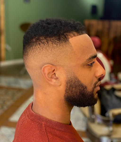 A high fade haircut with lined up beard of a man from the side